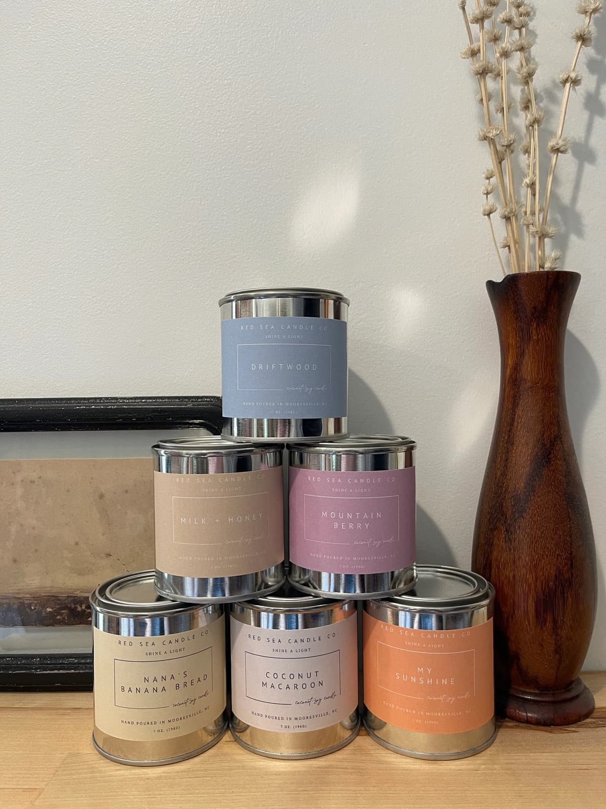 A stack of Red Sea Candle Co. candle tins beside a vase of dried flowers